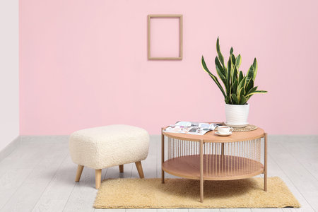 Pouf, coffee table with plant, magazine and cup of tea near pink wall in roomの写真素材