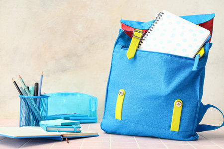 Blue backpack with school supplies on table against white grunge wall
