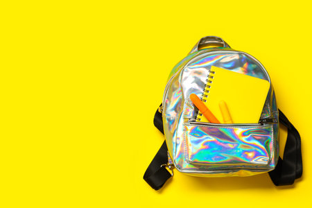 Backpack with stationery on yellow background. Top view