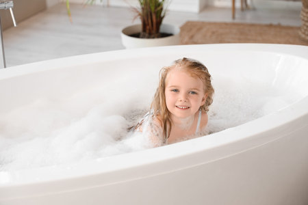 Cute little girl with foam taking bath in bathroomの写真素材