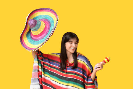 Young woman with sombrero, colorful poncho and maracas on yellow background. Cinco de Mayo celebrationの写真素材