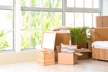 Cardboard boxes with things near window in bedroom on moving day