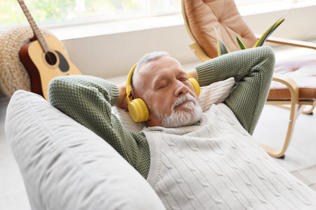 Mature man in headphones listening to music on sofa at home, closeup