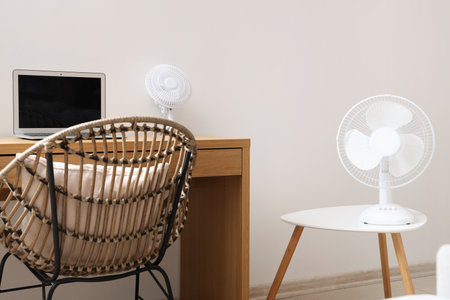 Modern electric fan and laptop on desk at home officeの写真素材