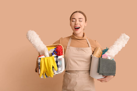 Young woman holding basket and bucket with cleaning supplies on beige backgroundの写真素材