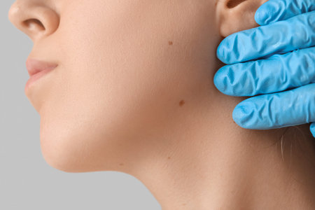 Dermatologist examining moles on woman's face against gray background, closeup