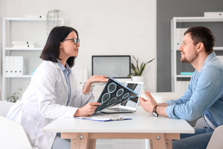 Female doctor with MRI scan talking to patient at table in clinic