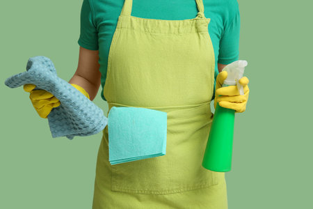 Woman in apron with spray bottle and rag on green background, closeupの写真素材