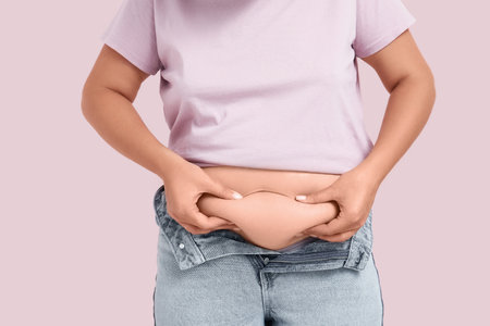 Overweight woman in tight jeans on pink background. Excess weight conceptの写真素材