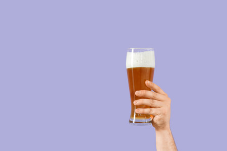 Hand with glass of beer on lilac backgroundの写真素材