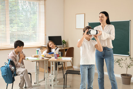 Female teacher putting VR glasses on pupil in classroomの写真素材
