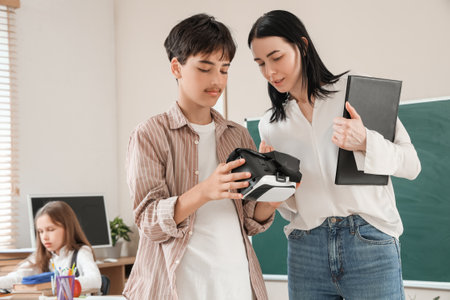 Teenage boy with VR glasses and teacher in classroomの写真素材