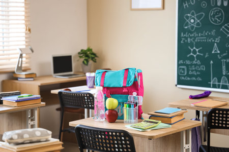 Apples with water bottle and backpack on desk in classroom