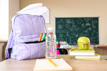 Apple with eyeglasses, books and backpack on desk in classroomの写真素材