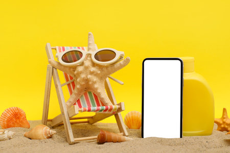 Mobile phone and beach accessories with mini deck chair, starfish and sunglasses on sand against...