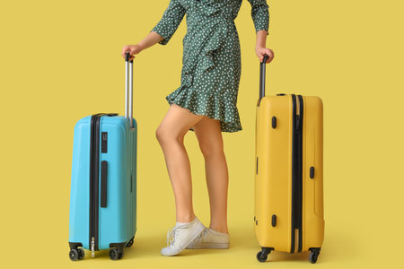 Young woman with suitcases on yellow backgroundの写真素材