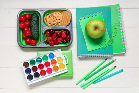 School supplies, lunch box with berries and cookies on white wooden background. Top view