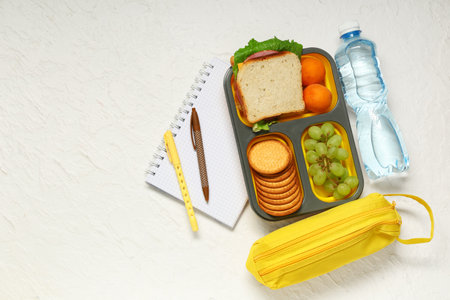Lunch box with tasty food, bottle of water and school supplies on white background. Top viewの写真素材