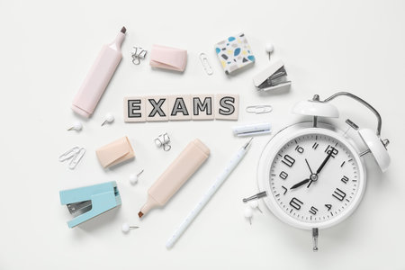 Composition with word EXAMS, alarm clock and different stationery on white backgroundの写真素材