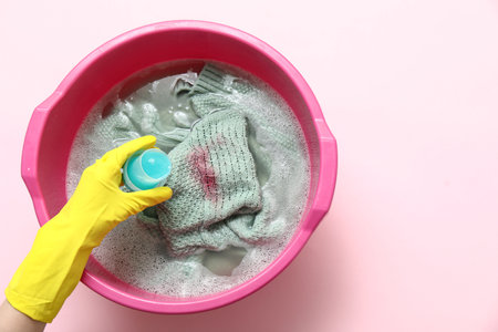 Woman in rubber gloves adding laundry detergent to clothes in plastic basin on pink backgroundの写真素材