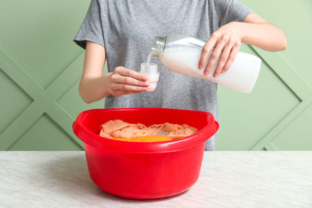 Woman adding detergent to clothes in plastic basin on table against green background