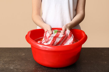 Woman washing clothes in plastic basin on table against beige backgroundの写真素材