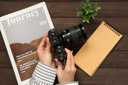 Female hands with professional photo camera, notebook and magazine on dark wooden background,...