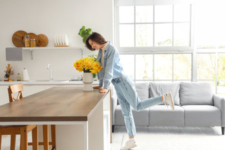 Young woman with daffodils on table in kitchenの写真素材