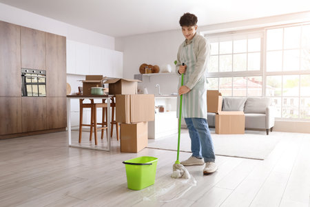 Young man mopping floor in kitchen on moving dayの写真素材