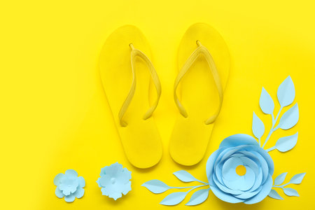 Composition with stylish flip-flops and beautiful paper flowers on yellow backgroundの写真素材