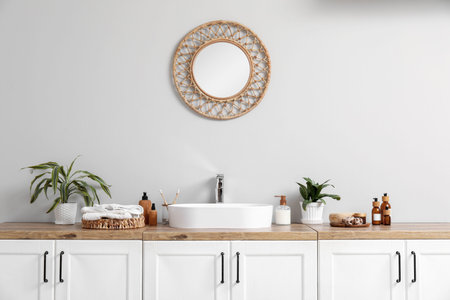 Modern sink, bath supplies on chest of drawers and mirror on light wall in bathroom