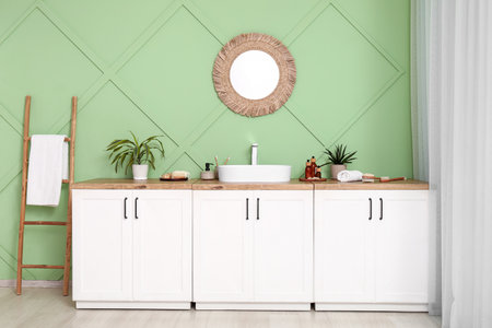 Stylish interior of bathroom with mirror, chest of drawers and sink near green wallの写真素材
