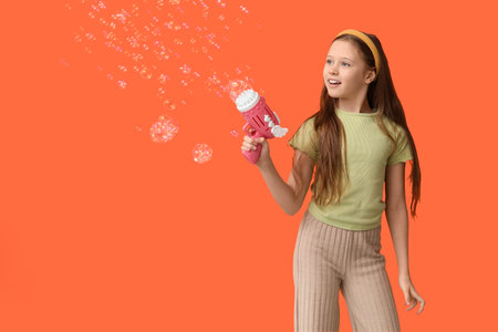 Cute girl with soap bubble gun on orange background