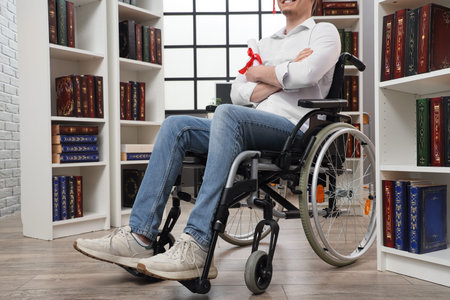 Male graduate in wheelchair with diploma at library