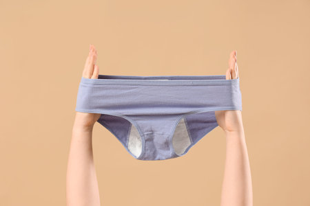 Female hands with period panties on beige background