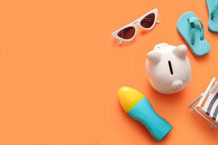 Piggy bank, sunglasses, sunscreen and decorative flip-flops on orange backgroundの写真素材