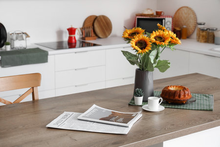 Sunflowers in vase near cup of coffee, cake and magazine on counter in kitchenの写真素材