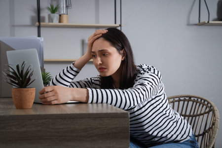 Depressed young woman sitting near table at home