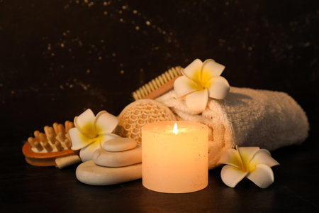 Beautiful spa composition with burning candle and tropical flowers on dark backgroundの写真素材
