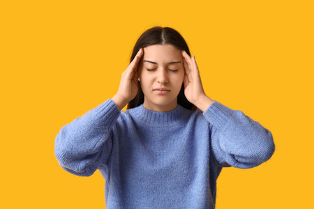 Beautiful young woman suffering from headache on yellow backgroundの写真素材