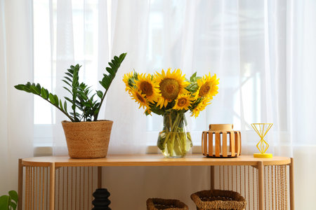Vase with beautiful sunflowers and houseplant on shelving unit in roomの写真素材