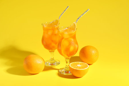 Glasses of spritz cocktail and oranges on yellow background
