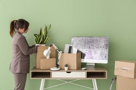 Businesswoman packing plant into moving box near green wall in office