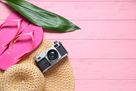 Stylish flip-flops, hat, photo camera and green leaf on pink wooden backgroundの写真素材