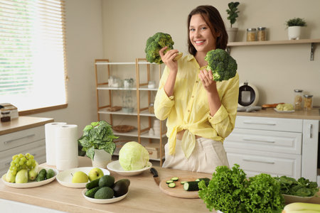 Beautiful young happy woman with broccoli and different fresh green vegetables in kitchenの写真素材