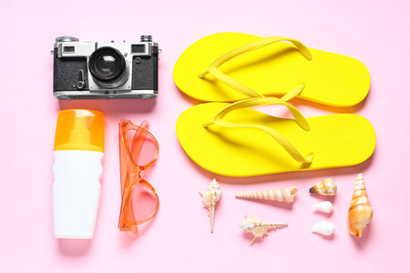 Flip-flops, photo camera, sunglasses, bottle of sunscreen and seashells on pink backgroundの写真素材