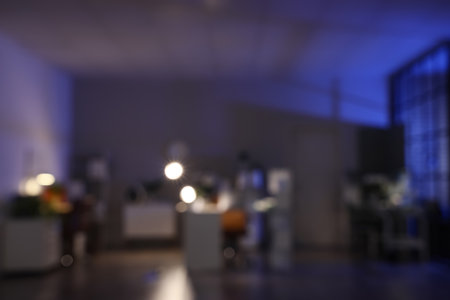 Blurred view of dark office with desks, shelf units and glowing lampsの写真素材