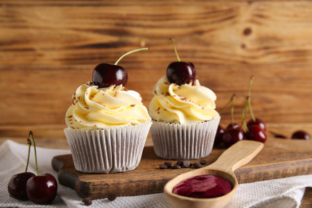 Board with sweet cherry cupcakes and spoon of jam on wooden backgroundの写真素材