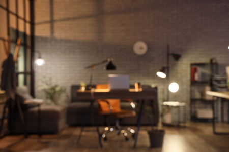 Blurred view of dark office with workplace, sofa and glowing lampsの写真素材