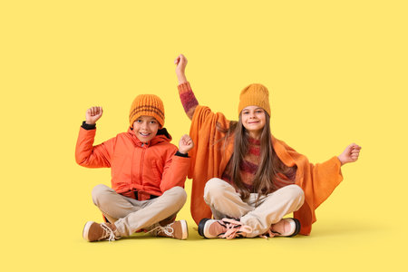 Cute little happy children in winter clothes on yellow backgroundの写真素材